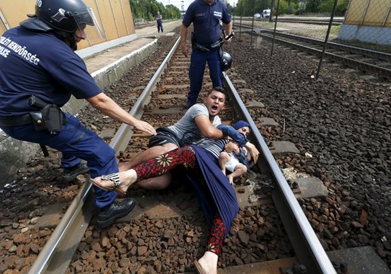 Унгарски полицай стои до семейство имигранти, поискали да избягат от жп гарата в унгарския град Витшке към центъра на града/Септември