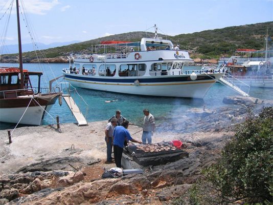 Екипажи на яхти пекат пържоли на скари за туристите по време на еднодневна екскурзия до съседен на Крит остров.