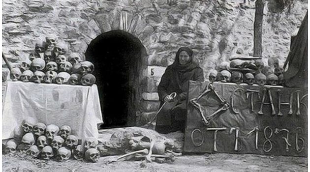 Марга Горанова, оцеляла след Баташкото клане, пред входа на църквата, където е извършено клането. С кости е написано “Останки от 1876 г.”.
