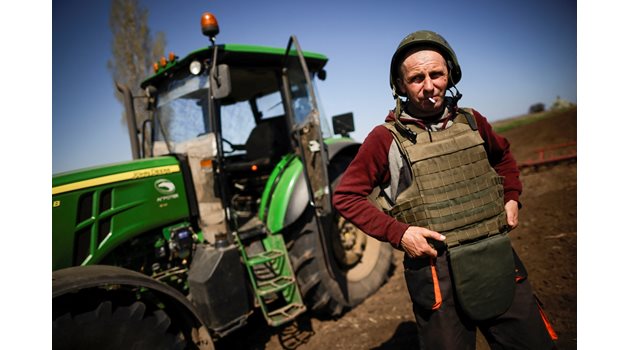 Украински фермер облича бронежилетка и шлем, преди да излезе да работи на полето в Запорожка област.

