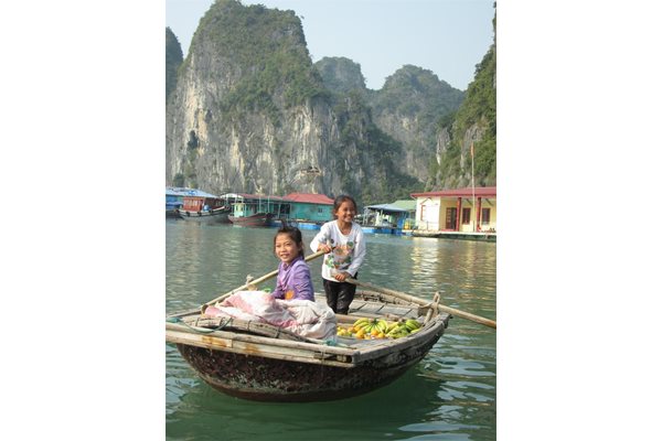 Момичета с лодка продават плодове на туристите в залива Халонг.