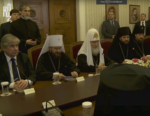 Кадър от видеото на руската патриаршия. Вляво прав с телефон в ръка протойерей Николай Георгиев записва.