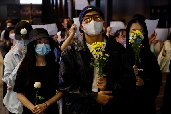 Едни държат цветя, а други - бели листове хартия в знак на протест срещу ограниченията на коронавирусната болест (COVID-19) в континентален Китай, по време на възпоменание на жертвите на пожар в Урумчи, в Хонконг. СНИМКА: РОЙТЕРС