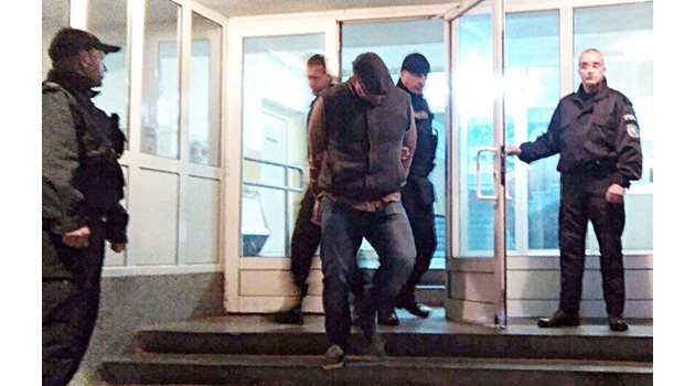 Полицаи извеждат Божо от сградата на ОДМВР в Бургас. Той крие лицето си под козирката на каскет. Снимка: Елена Фотева