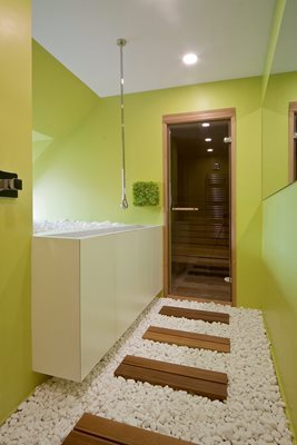 СПА зоната с душ и сауна. В предверието - мивка със смесител, спускащ се от тавана, и декорация с камъни и дърво на пода.