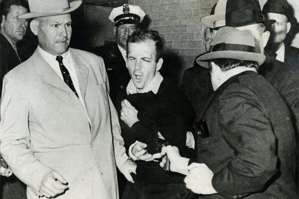 Лий Харви Осуалд (в средата) получава от упор куршум в корема от Джак Руби (вдясно).
