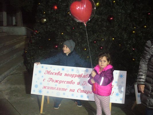 Деца се снимат край надписа, който уведомява, че Москва поздравява сърдечно жителите на Стара Загора с коледните и новогодишните празници.