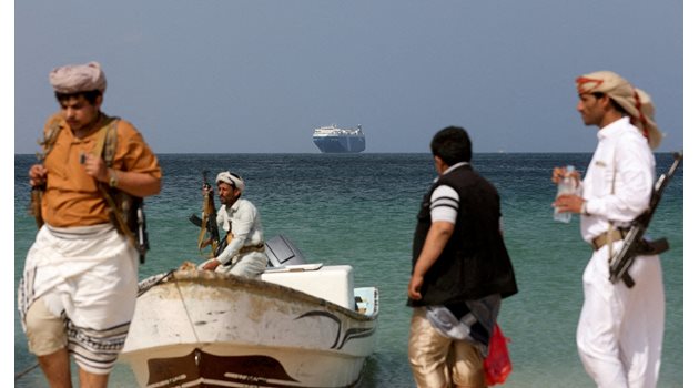 Въоръжени мъже на брега на Червено море, в далечината е акостирал Galaxy Leader. Корабът бе похитен от йеменски хути на 19 ноември 2023 г. и се превърна в туристическа атракция. 
СНИМКА: РОЙТЕРС