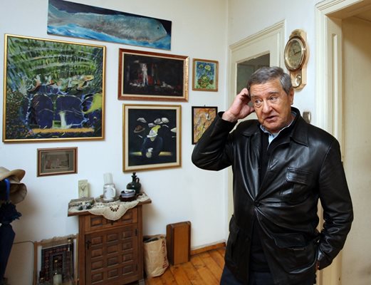 Проф. Боян Биолчев пред стената в дома си, покрита с картини от негови приятели художници