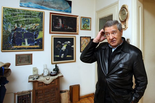 Проф. Боян Биолчев пред стената в дома си, покрита с картини от негови приятели художници