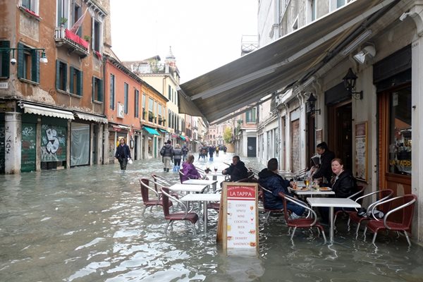 Туристи седят в ресторант на наводнена улица.