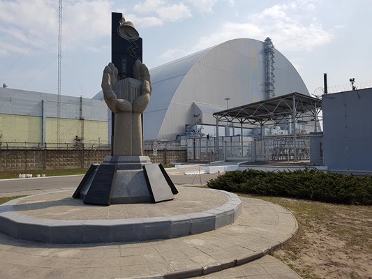 Паметникът на жертвите, загинали заради “Чернобил”. Вдясно е четвърти реактор, покрит със саркофаг.