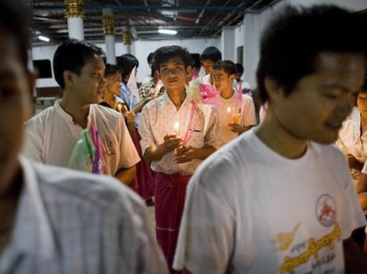 Мъже вървят със запалени свещи към пагодата за молитва.