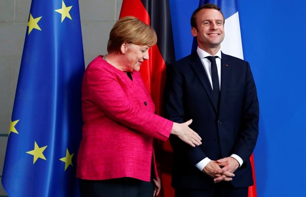 Френският президент се усмихва на журналистите и не забелязва, че Меркел му подава ръка.