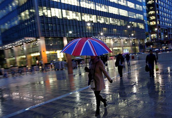 Британци вървят под дъжда в новото сити Канари Уорф на Лондон.  СНИМКА: РОЙТЕРС