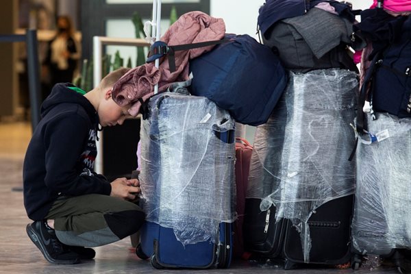 Младеж с куфари чака на летище преди полет.