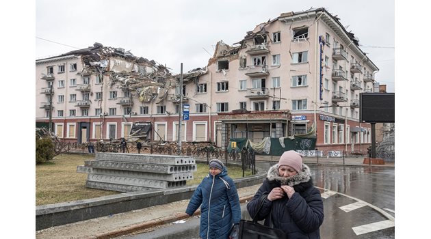 Жени вървят по улица пред разрушена сграда в Чернигов.

