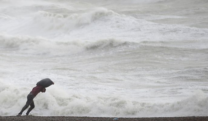 Мъж се бори с вятъра на плаж в Нюхевън, Южна Англия.