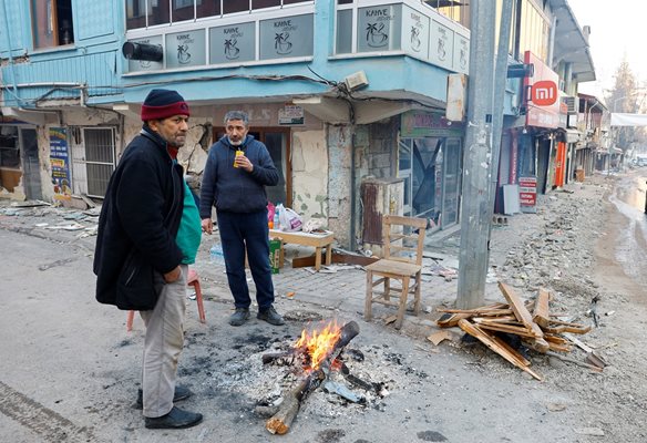 Мъже се топлят около огъня в разрушения Пазарджък. СНИМКА: РОЙТЕРС