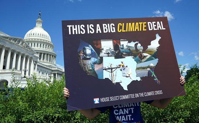 Активист пред Конгреса държи плакат, подкрепящ климатичните амбиции на САЩ.
