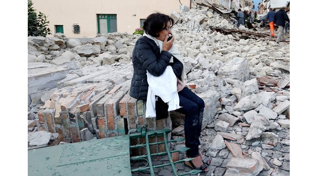 Притеснена жена седи сред останките от рухналия и? дом.