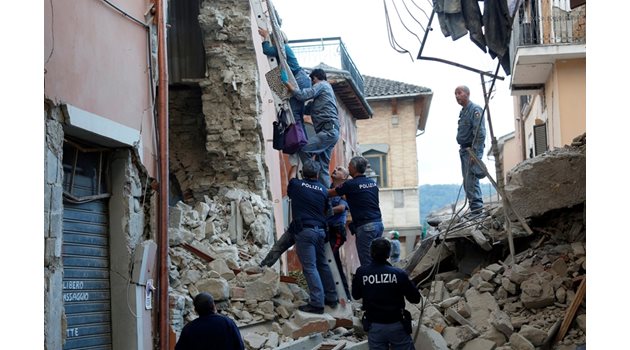 Полицаи и доброволци помагат на жена да излезе по стълба от унищожения си дом.
