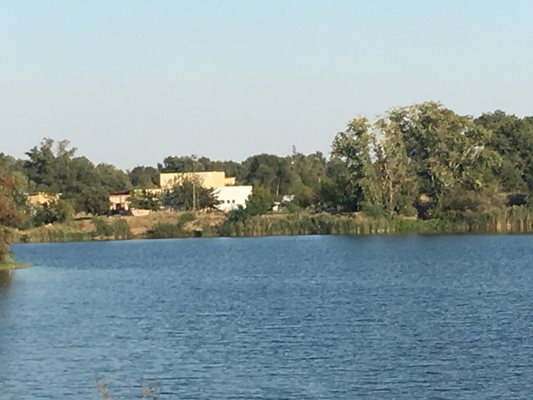 Езерото край селото, зад което има различни постройки, които са недостъпни, тъй като са частни.