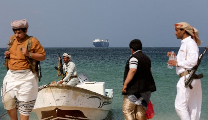 Въоръжени мъже на брега на Червено море, в далечината е акостирал Galaxy Leader. Корабът бе похитен от йеменски хути на 19 ноември 2023 г. и се превърна в туристическа атракция. 
СНИМКА: РОЙТЕРС