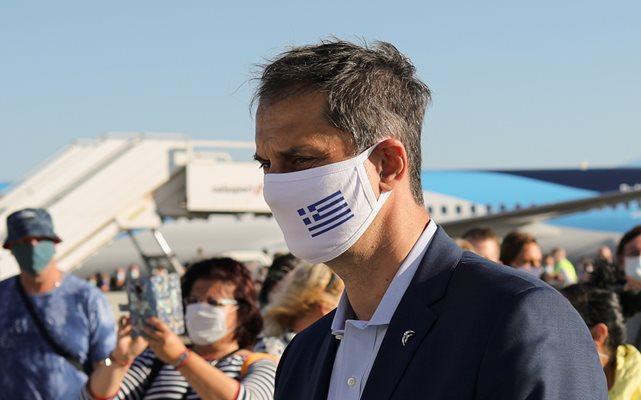 Гръцкият министър на туризма Хари Теохарис с маска ма лицето посреща германски туристи.