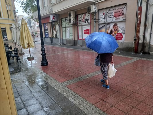 Жена върви смело с чадъра и покупките си.