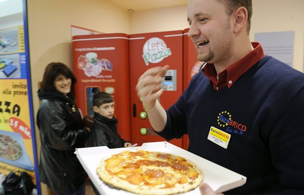 Мъж яде пица в Италия, купена от автомата отзад. Машината опича за 3 минути избраната пица.