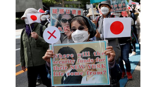 Японци протестират срещу решението на Мако и Кеи да се оженят. Жената на преден план носи плакат: “Откъде ще дойдат парите за сигурността им по време на новия им живот в Ню Йорк?”.