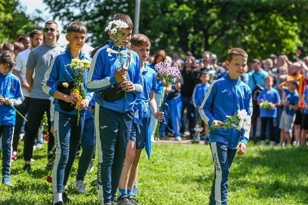 Деца от школата изчакват реда си, за да оставят цветя на паметника на могилката.