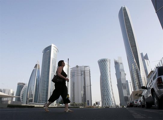 Жена пресича улица “Ал Вахда” в столицата на Катар Доха. Там  са разположени супермодерни небостъргачи за милиони долари, в които се помещават офисите на богати  компании и банки.