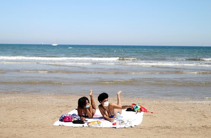 Жени с маски се пекат на плаж в Испания.