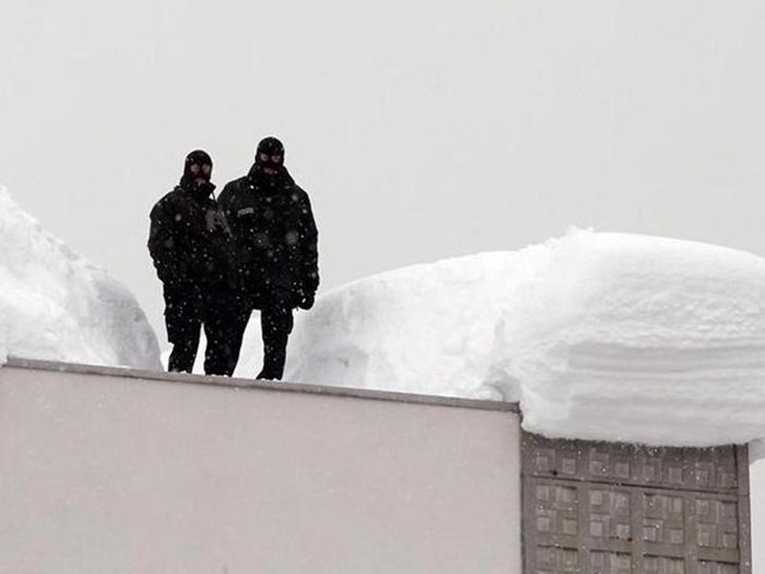 Охранители вардят зоната за сигурност от заснежения покрив на конгресния център в Давос.
